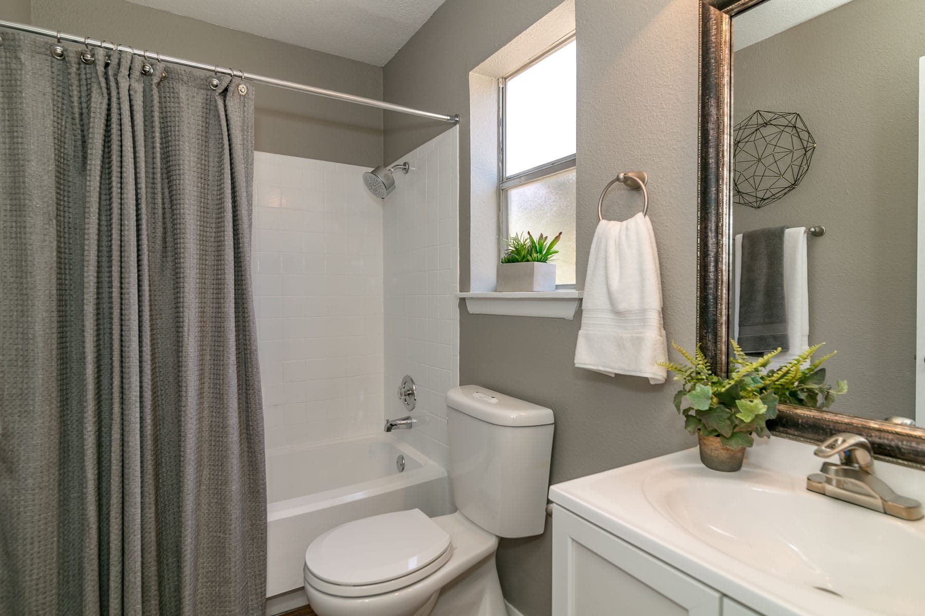 Apartments for Rent San Antonio TX - City-Base Vista - Modern Bathroom With a Tall Mirror and Sink, an Obscured Styled Window, and a Shower With a Curtain