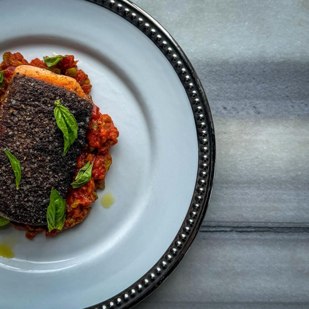 Elegant gourmet salmon served on a rustic tomato sauce at City Base Vista in San Antonio, Texas, garnished with fresh basil leaves.